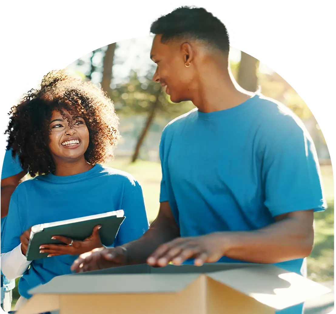 Two volunteers smiling while packing boxes in a park.